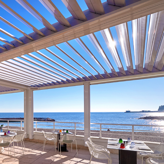 Sonnige Terrasse eines Restaurants am Strand mit einem Lamellendach